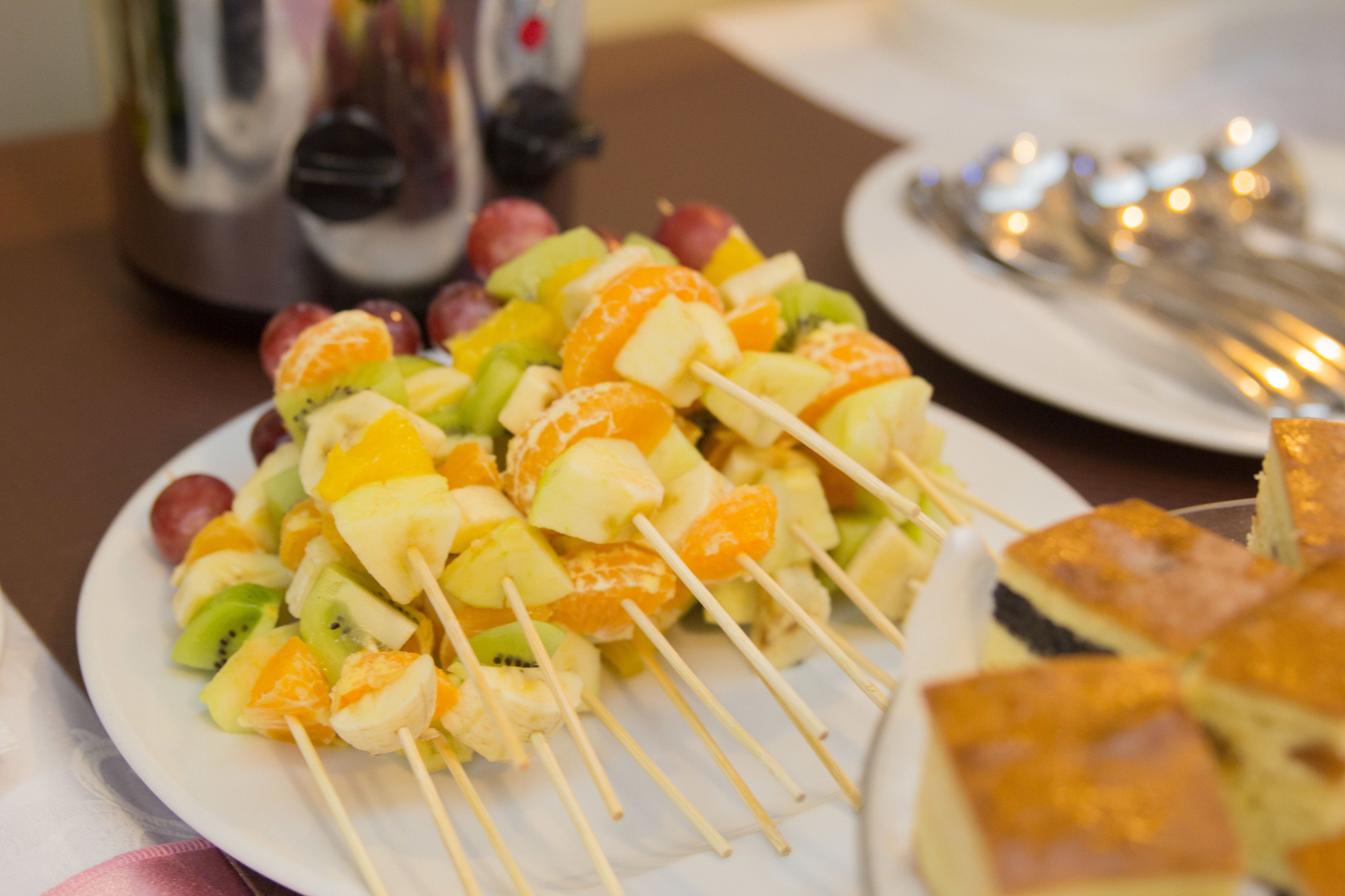 A plate of fruit skewers with various fruits like kiwi, orange, and grapes.