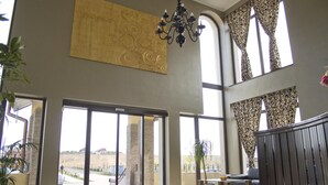 Un hall d’entrée spacieux, doté de grandes fenêtres, d’un lustre et offrant une vue sur l’extérieur.