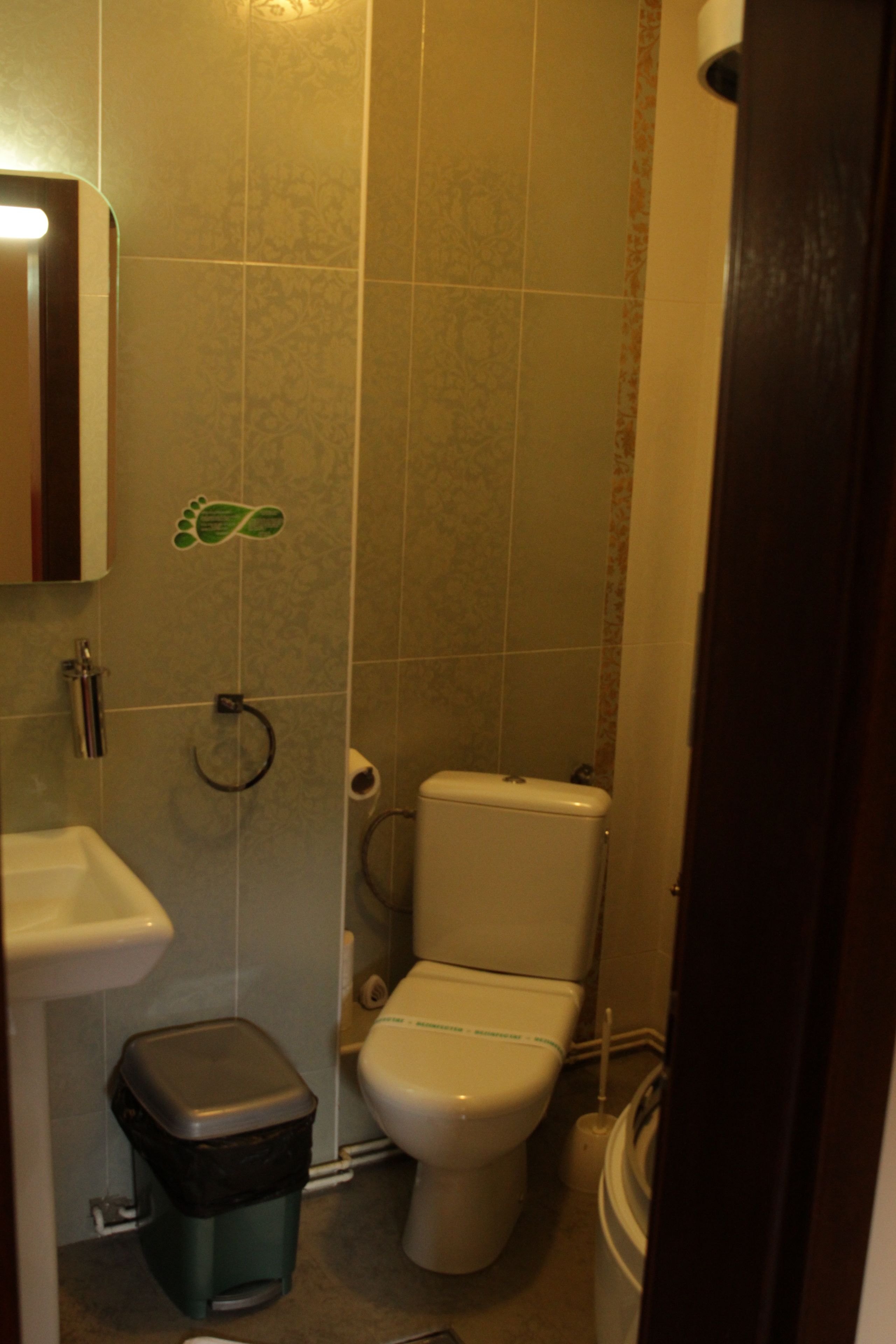 Un baño con inodoro, lavamanos, cubo de basura y un adhesivo en el suelo en la pared.