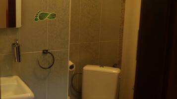 Un baño con inodoro, lavamanos, cubo de basura y un adhesivo en el suelo en la pared.