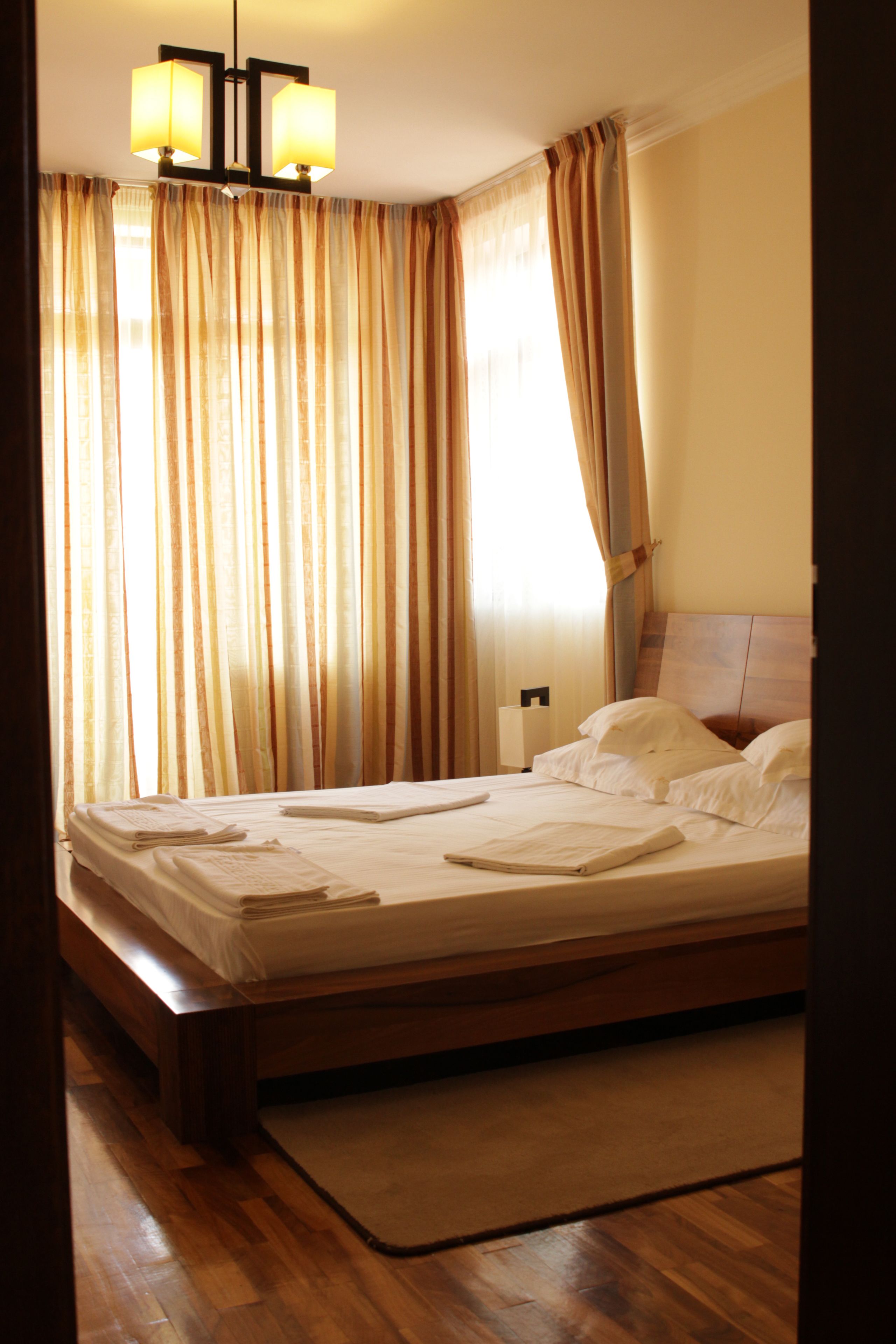 Una cama bien hecha con sábanas blancas, un cabecero de madera y una mesita de noche con una lámpara.