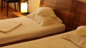 A hotel room with two single beds, a nightstand with a lamp, a chair, and a wooden headboard.