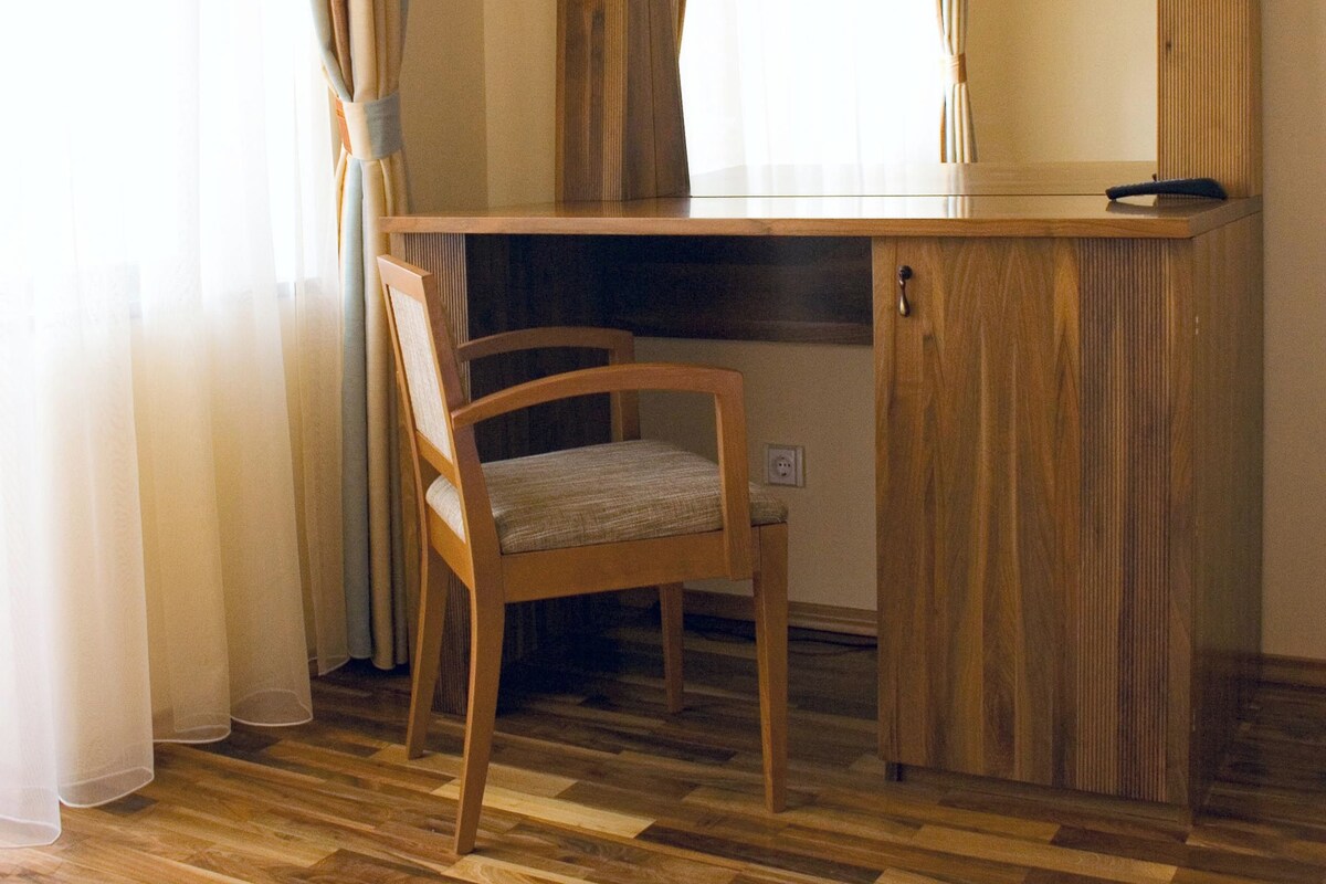 A room with a wooden desk, a chair, a large mirror, and a window with curtains.