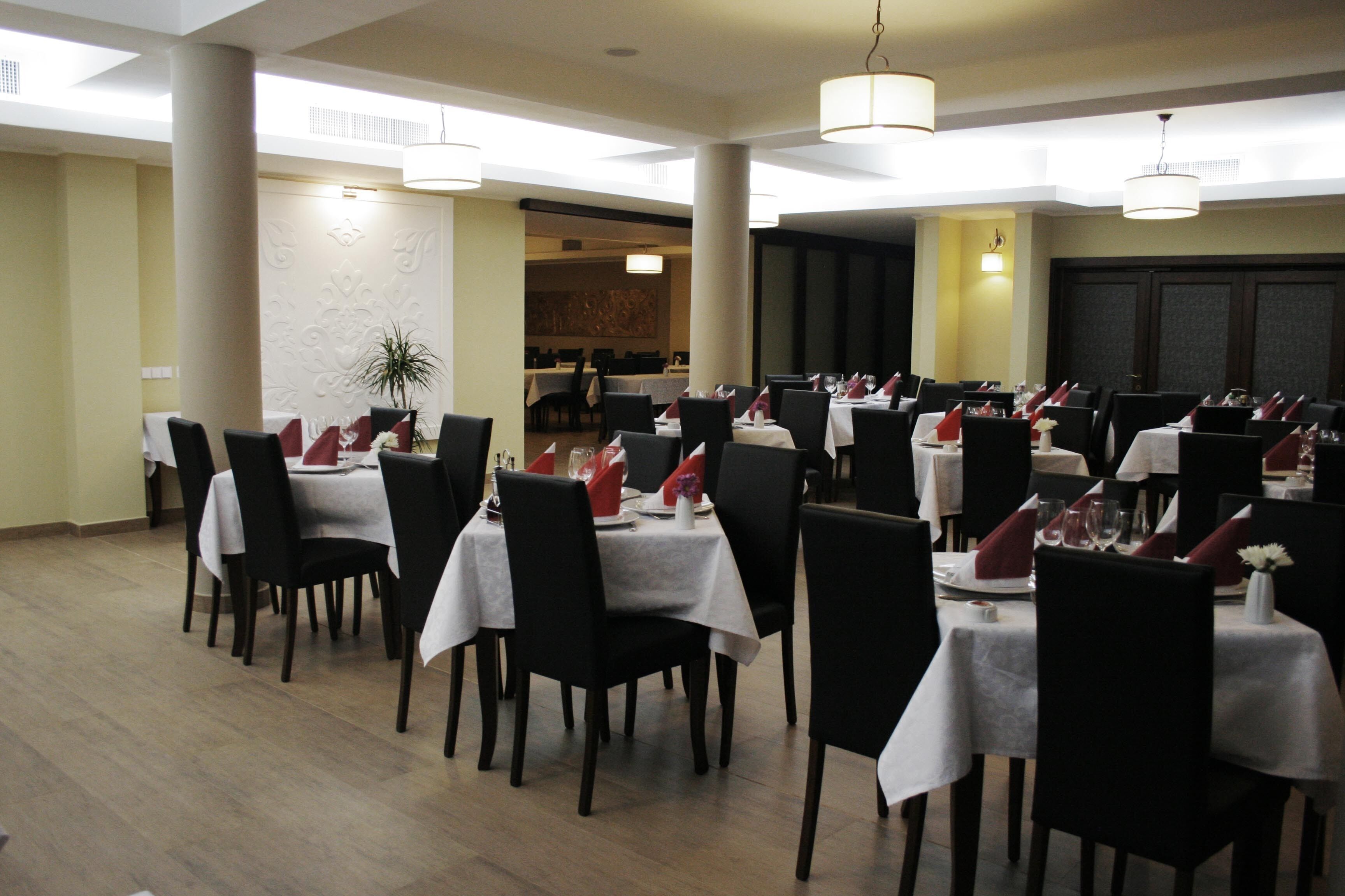 A dining area with multiple tables set for service, featuring white tablecloths and red napkins.