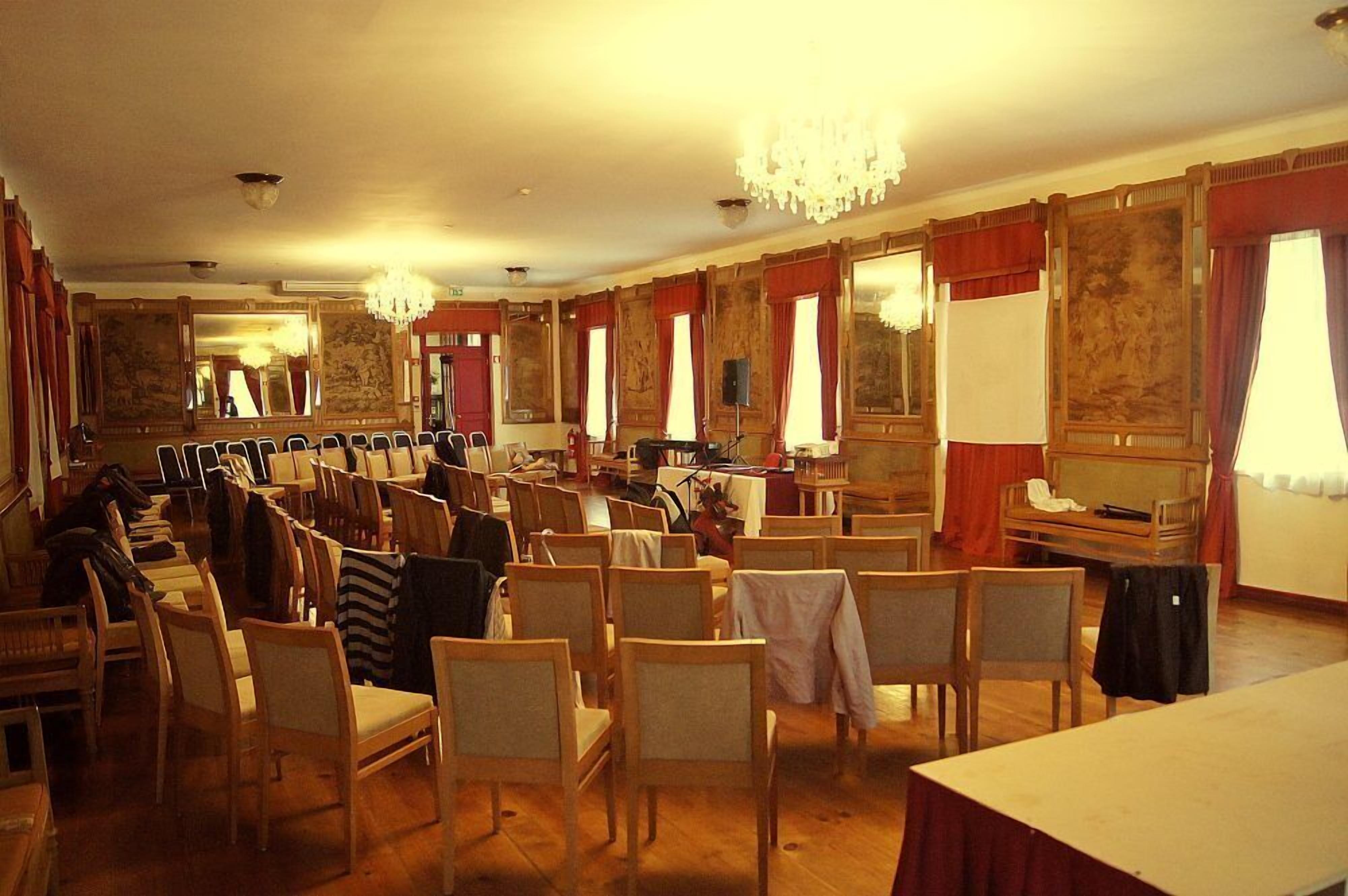 Une chambre d’hôtel avec des chaises en bois disposées en rangées, un lustre et un piano.