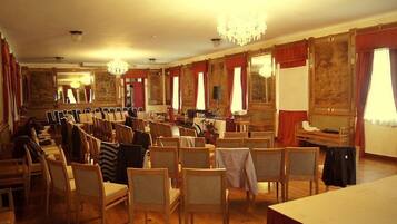 Une chambre d’hôtel avec des chaises en bois disposées en rangées, un lustre et un piano.