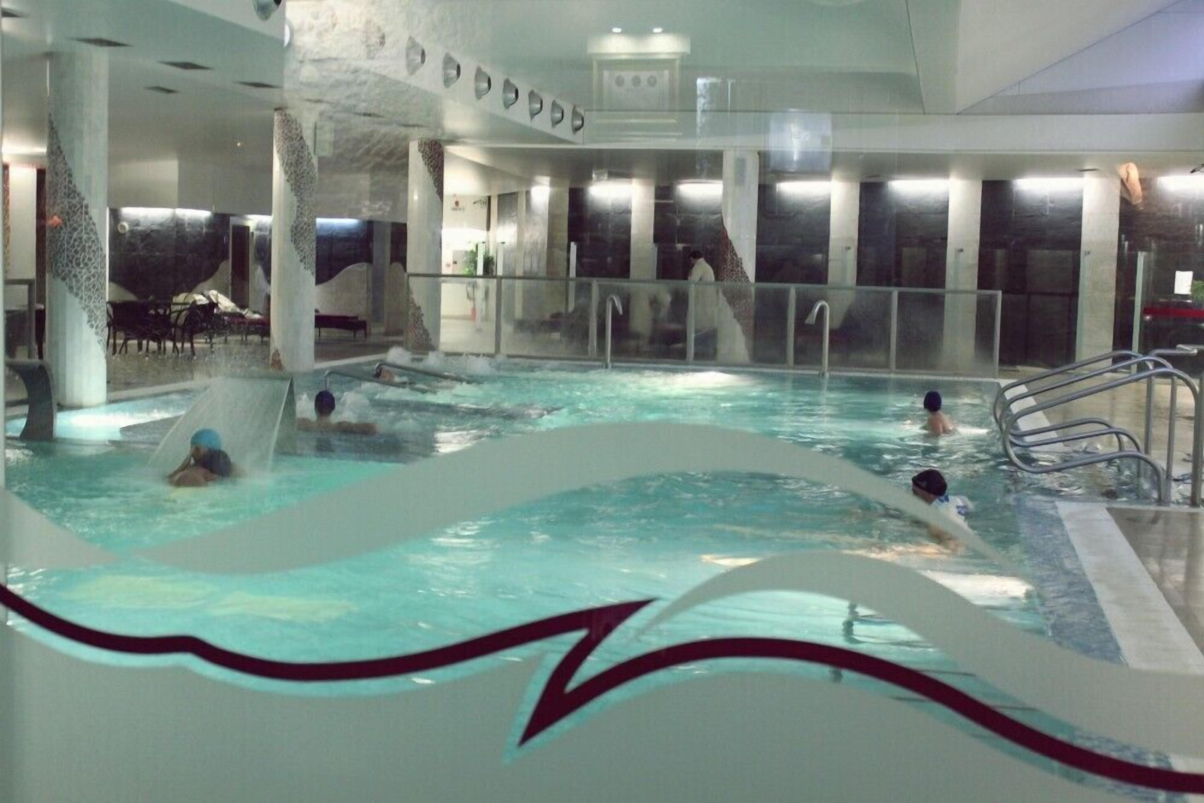 Une piscine intérieure dotée de plusieurs couloirs, d’un espace détente avec des chaises et d’une grande fresque murale.