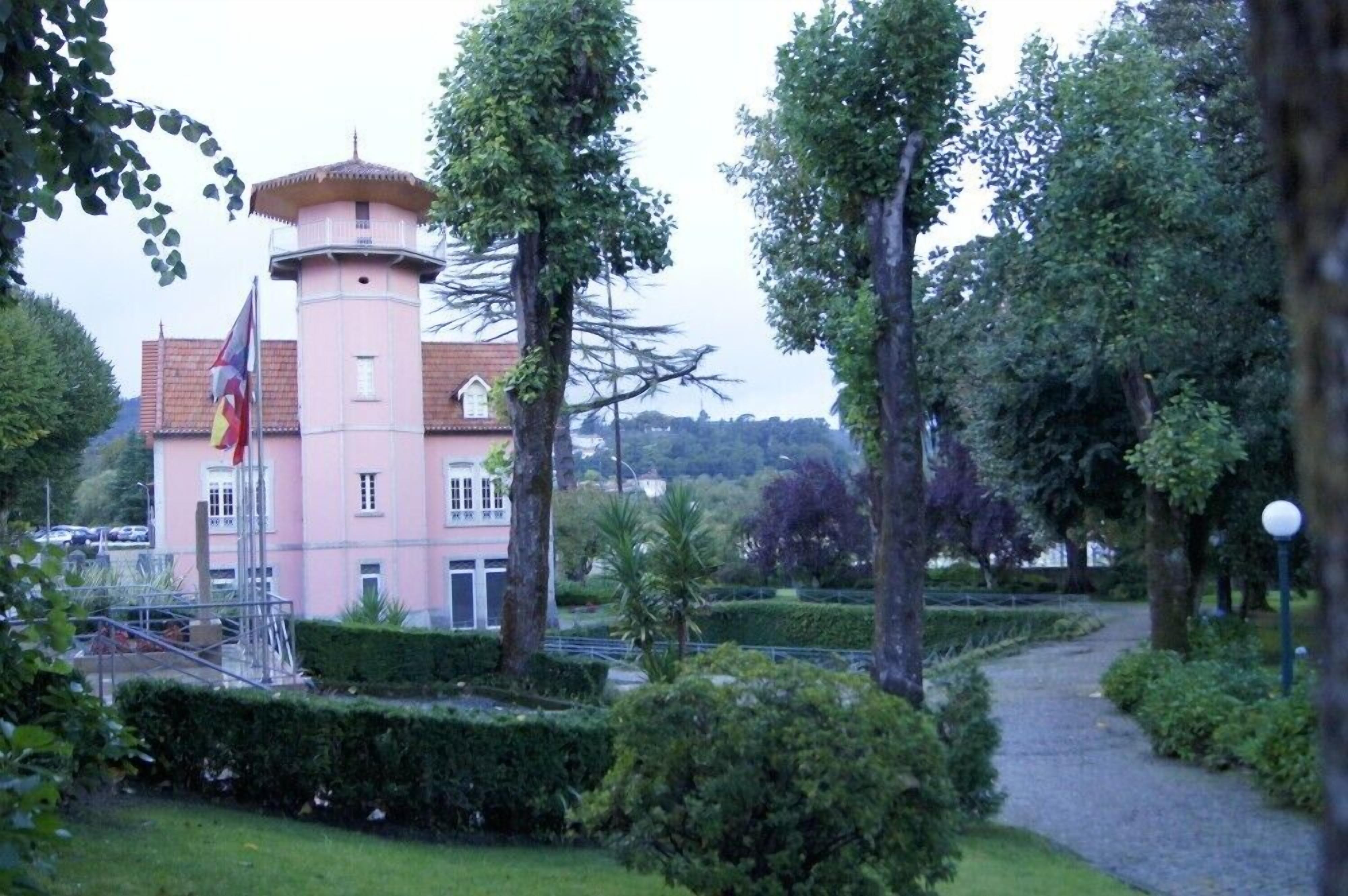 A pink building with a tower, surrounded by trees and a pathway.