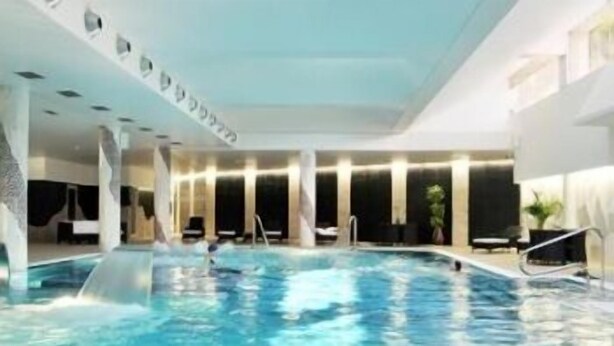 An indoor swimming pool with clear water, surrounded by lounge chairs and a modern architectural design. - Palace Hotel & Spa Termas de São Vicente (Penafiel)