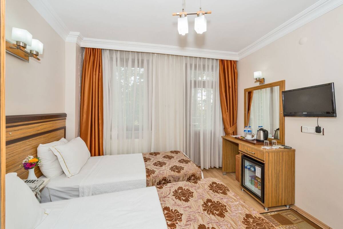 A hotel room with two beds, a desk with a television, and a minibar.