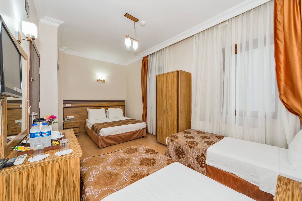 A hotel room with two beds, a wooden wardrobe, a desk with a mirror, and a television.