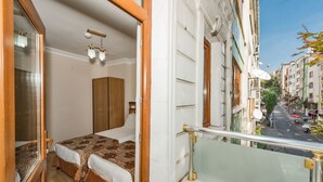 Un balcó amb barana de vidre que dona a un carrer amb edificis i cotxes aparcats.