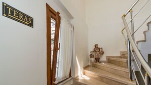 Una escala amb barana metàl·lica, una porta de fusta amb un cortinet blanc i un rètol que diu "TERAS".
