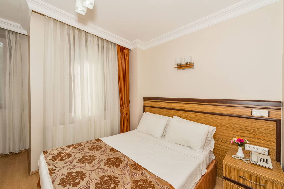 A hotel room with a large bed, a bedside telephone, and a small table with a vase of flowers.