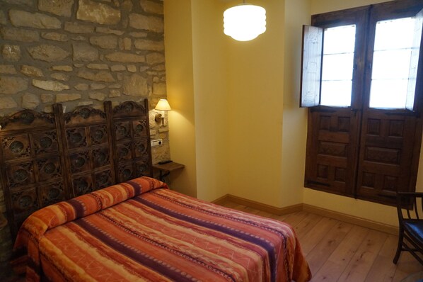 A room with a bed, a stone wall, a wooden door, and a window. - Arganzón Plaza (La Puebla De Arganzon)
