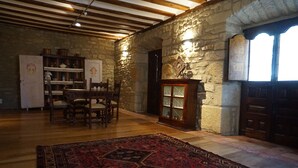 A rustic room with a wooden dining table, chairs, a red patterned rug, stone walls, and a wooden cabinet with glass doors. - Arganzón Plaza (La Puebla De Arganzon)