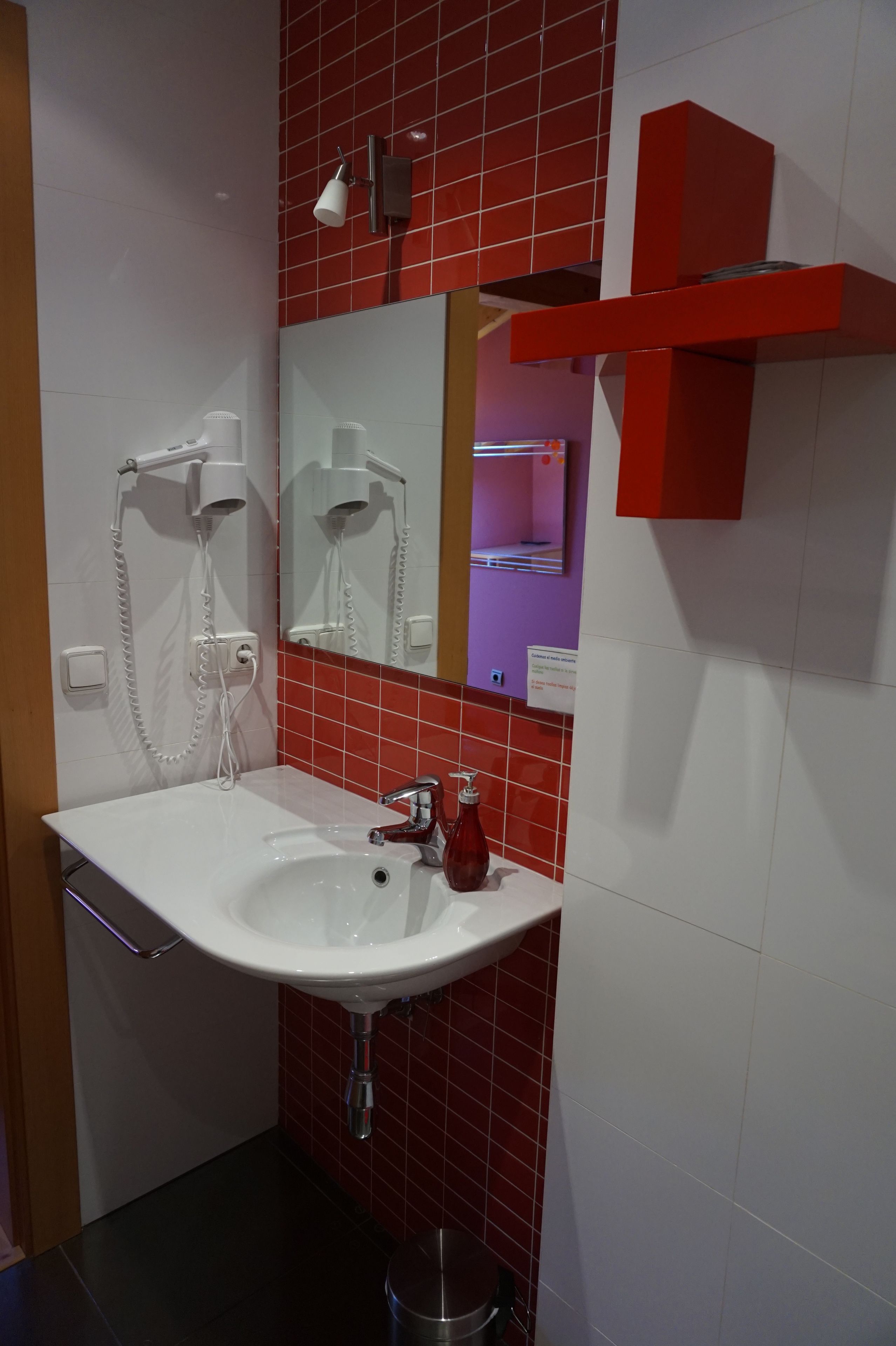 Ein Badezimmer mit einem weißen Waschbecken, einem Spiegel, einem roten Handtuchhalter und einem roten Regal.