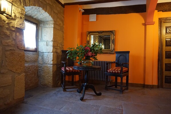 Une arche en pierre, une table avec un vase de fleurs, deux chaises, un miroir et un radiateur.