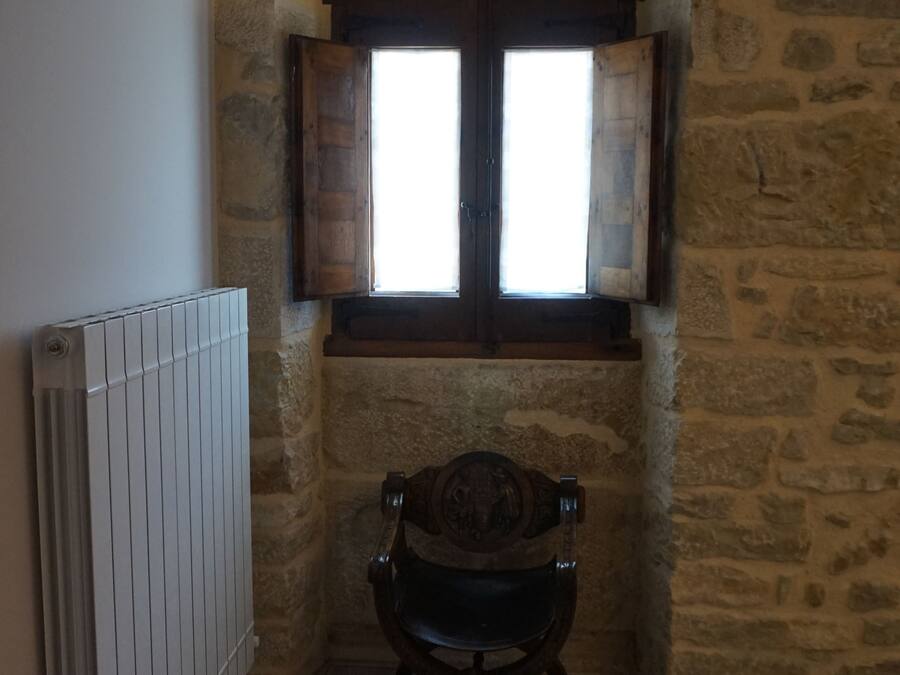 A stone-walled room with a wooden chair, a radiator, and a window with wooden shutters.