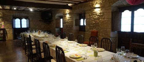 A long dining table set with chairs, surrounded by stone walls and wooden beams.