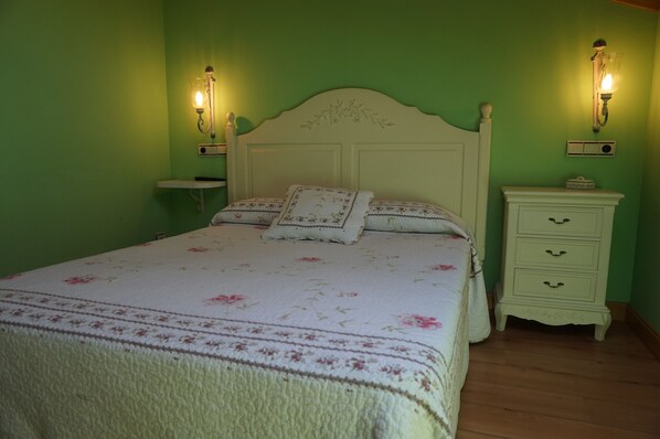 A bedroom with a floral bedspread, a white headboard, two bedside tables with lamps, and a nightstand with a radio. - Arganzón Plaza (La Puebla De Arganzon)