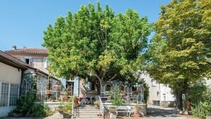 A courtyard with a tree, outdoor seating, and a staircase leading to a building. - La Table d'Antan (Bon-Encontre)