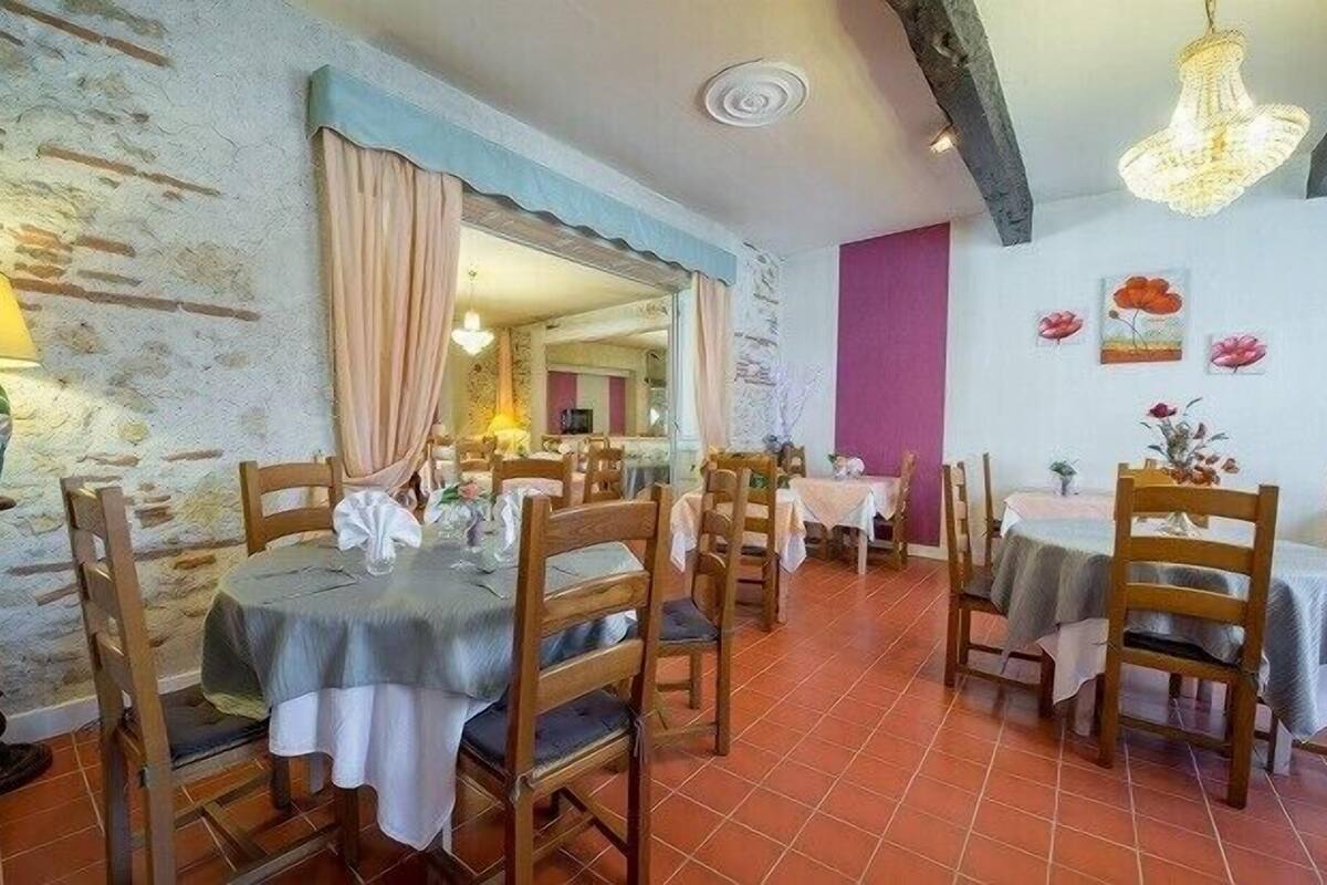 Un espace repas avec des tables et des chaises en bois, un mur en pierre et un lustre.