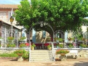 Un edificio de piedra con una reja de hierro forjado, escalones que conducen a un porche cubierto y macetas con plantas.