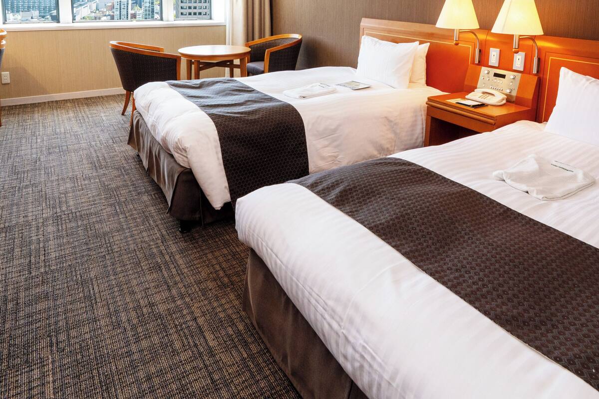A hotel room with two beds, a desk, and a view of the cityscape.
