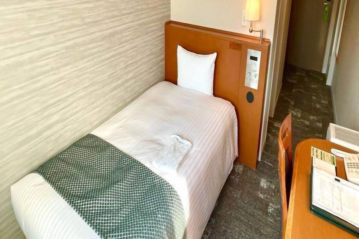 A single bed with a wooden headboard, a bedside table with a lamp, and a framed picture on the wall.