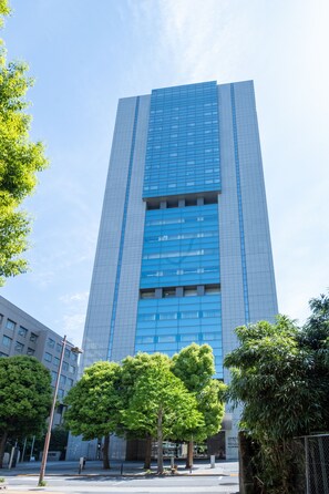 Un grand bâtiment moderne à la façade de verre, entouré d’arbres et surplombant un ciel dégagé.