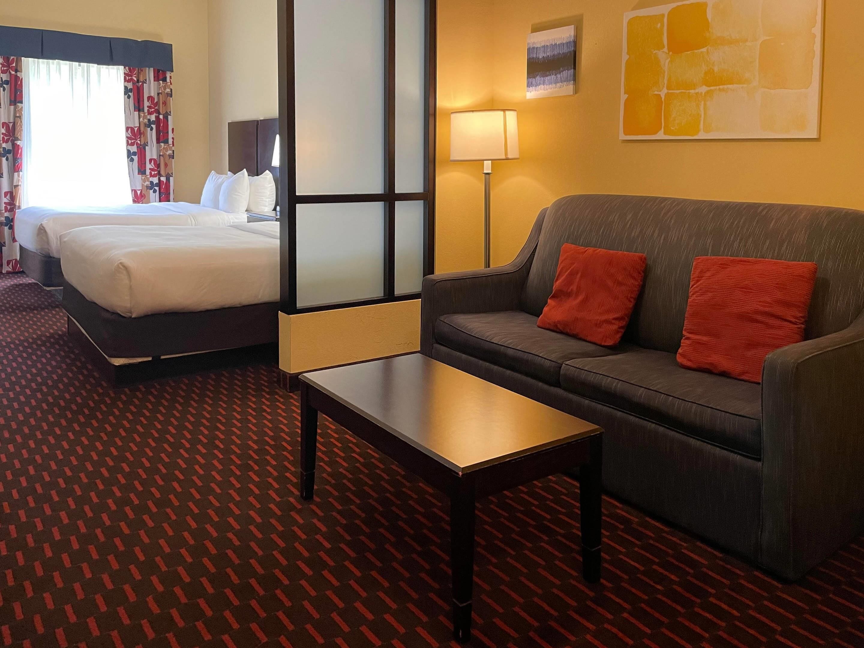 A hotel room with a bed, a sofa, a table, and a lamp.