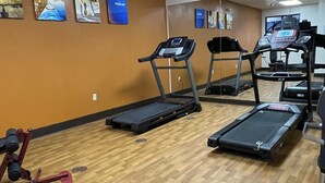 Un gimnasio con cintas de correr, una bicicleta estática y una máquina de ejercicios roja.