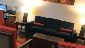 Habitación de hotel con sofá, escritorio con computadora y un cuadro en la pared.