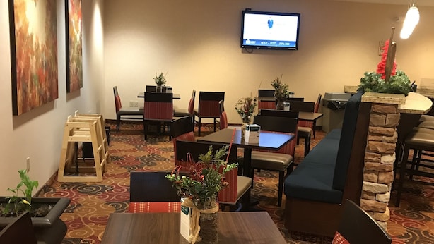 Un comedor de hotel con varias mesas y cabinas, un televisor de pantalla plana en la pared y plantas decorativas.
