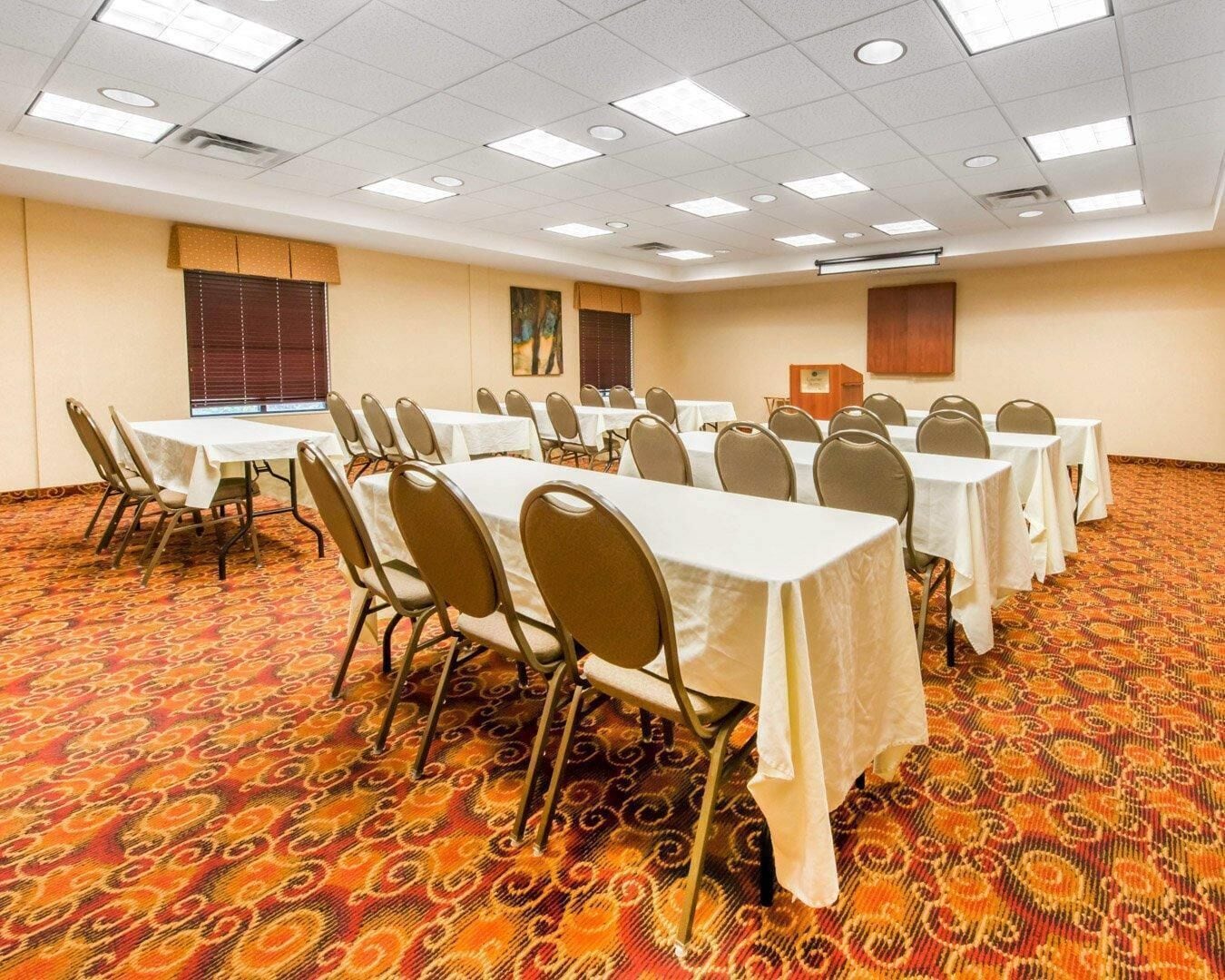 A conference room with multiple tables and chairs, carpeted floor, and ceiling lights.