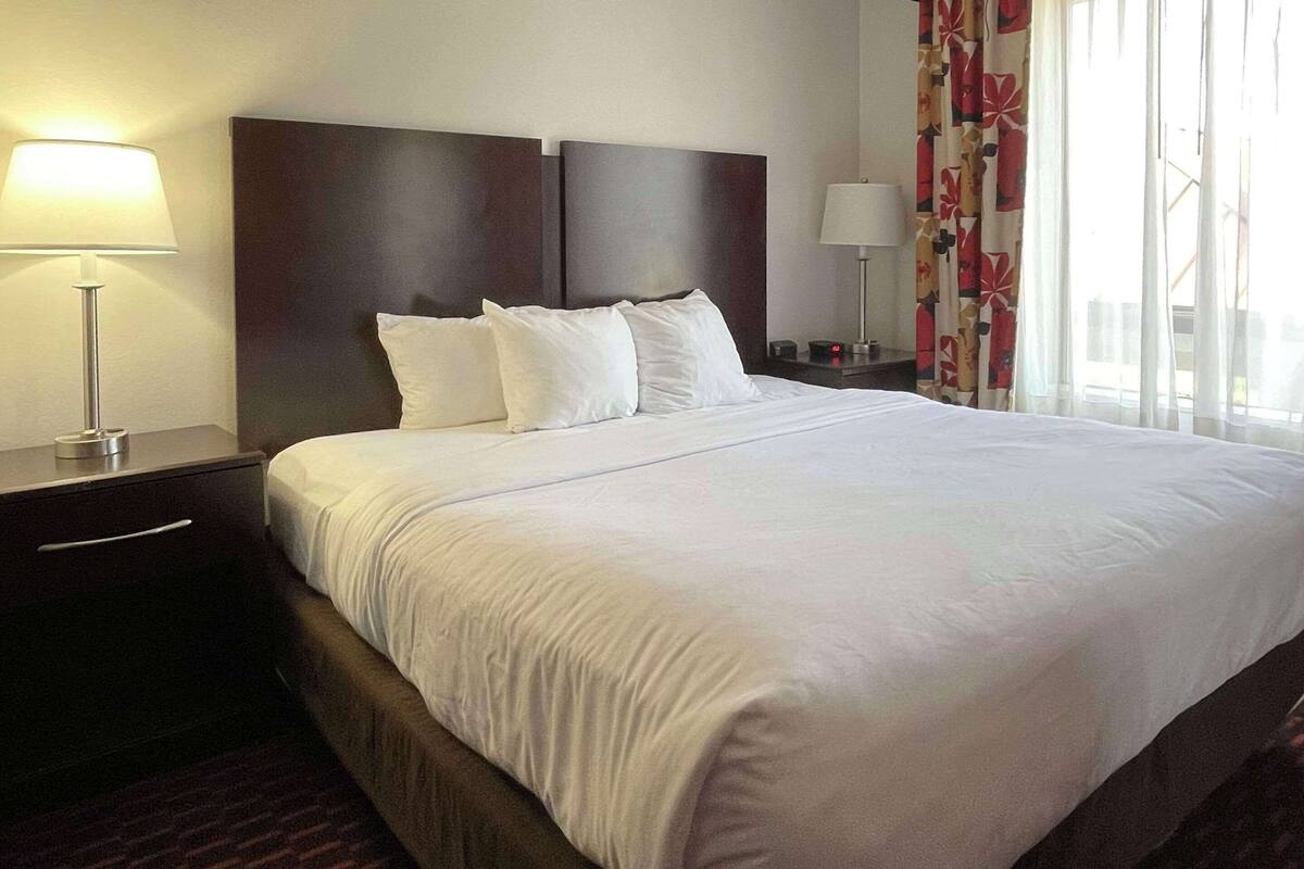 Ein Hotelzimmer mit einem großen Bett, zwei Nachttischen mit Lampen, einem Schminktisch und einem Fenster mit Vorhängen.