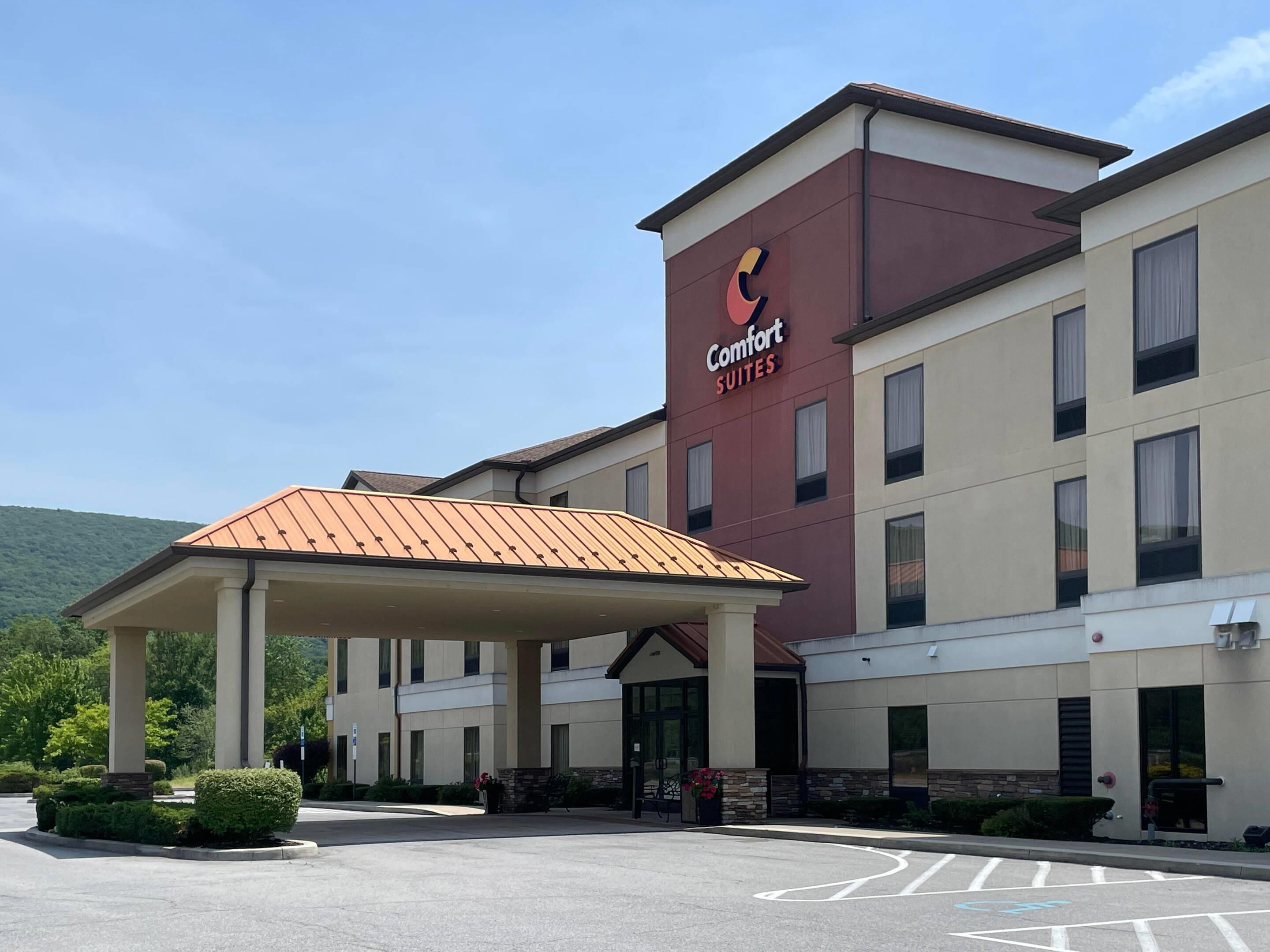 A Comfort Suites hotel with a covered entrance, a parking lot, and a mountainous backdrop.