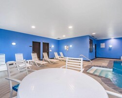 Zona de piscina con sillas de descanso y una mesa, rodeada de paredes y puertas azules.