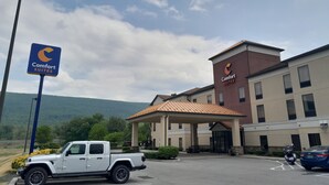 Un hotel Comfort Suites con estacionamiento, un SUV Jeep y montañas al fondo.