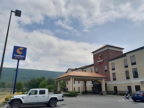 A Comfort Suites hotel with a parking lot, a Jeep SUV, and a mountain backdrop. - Comfort Suites Altoona North (Altoona)