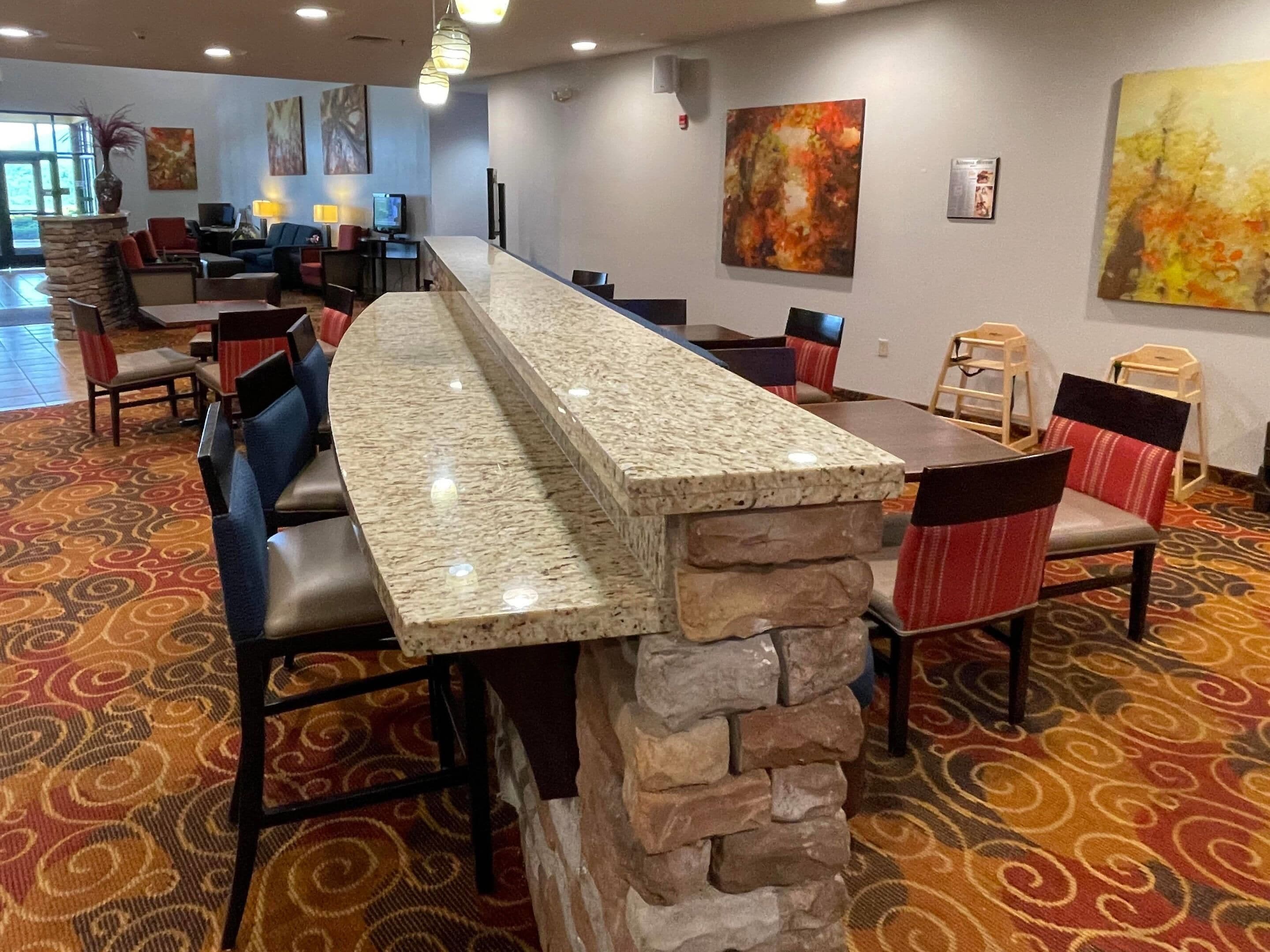 A long bar area with a stone accent, surrounded by chairs and tables, with artwork on the walls.