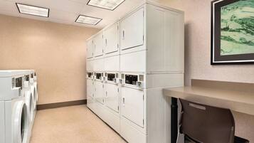 A laundry room with multiple white washers and dryers, a bench, and a framed artwork on the wall.