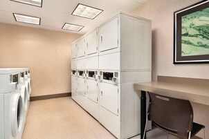 A laundry room with multiple white washers and dryers, a bench, and a framed artwork on the wall.