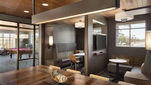 Una habitación de hotel moderna con mesa de billar, sofá, una mesita redonda y televisor.