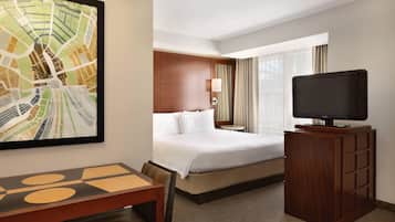 Une chambre d’hôtel avec un lit, un téléviseur posé sur un meuble en bois, un bureau avec des chaises et un tableau représentant un paysage urbain accroché au mur.