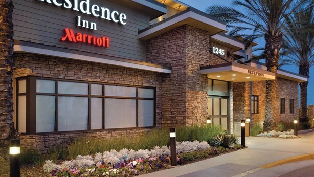 Exterior moderno de un hotel con fachada de piedra, ventanas amplias y una zona de recepción.