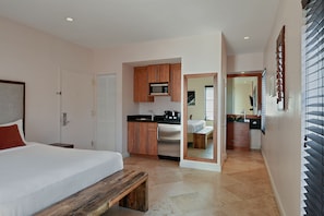 A bedroom with a bed, a wooden bench, a kitchenette with a microwave, and a bathroom visible through an open door. - Casa Victoria Orchid (Miami Beach)