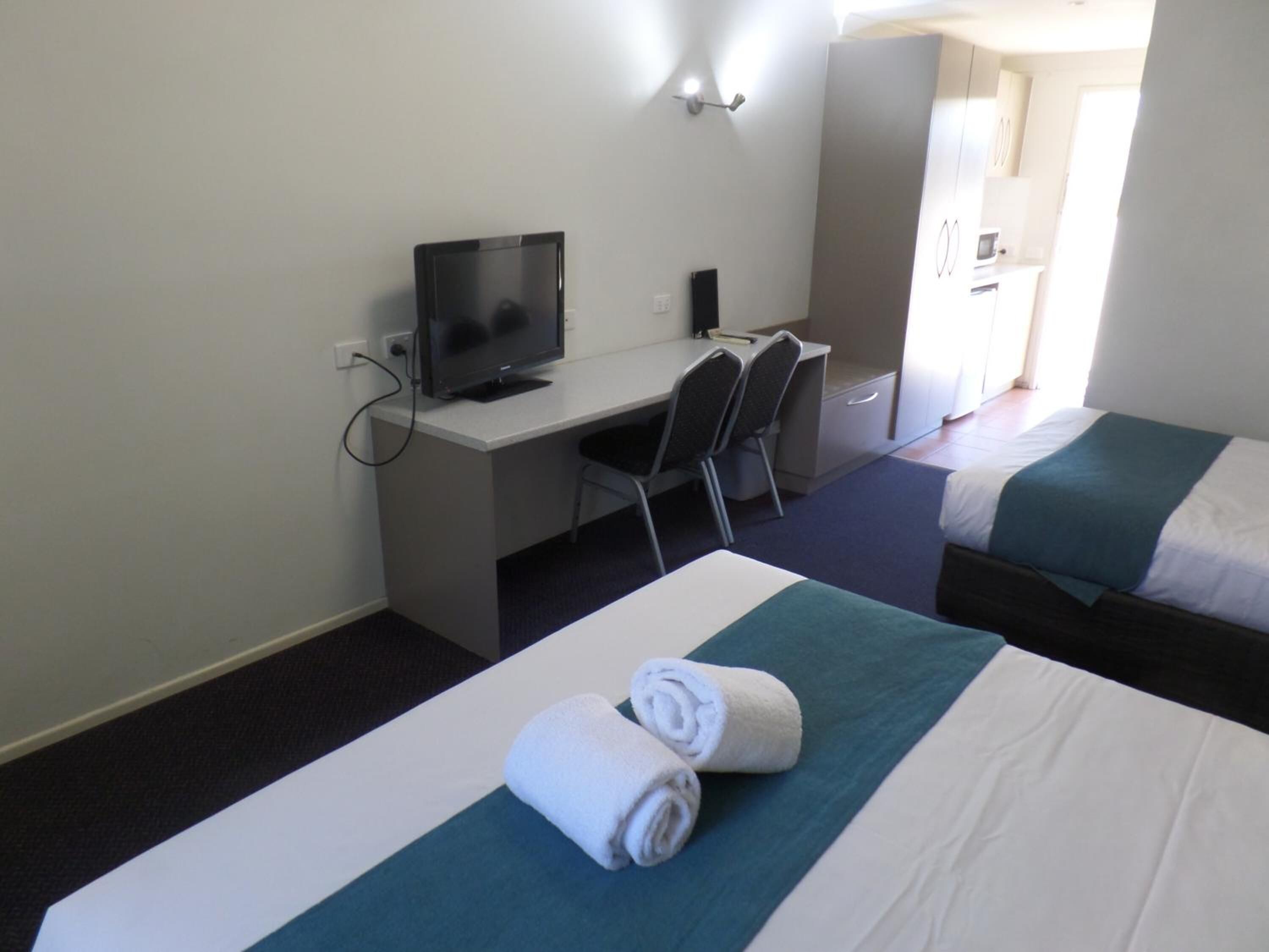 A hotel room with a desk, a television, two beds, and a bathroom visible through an open door.