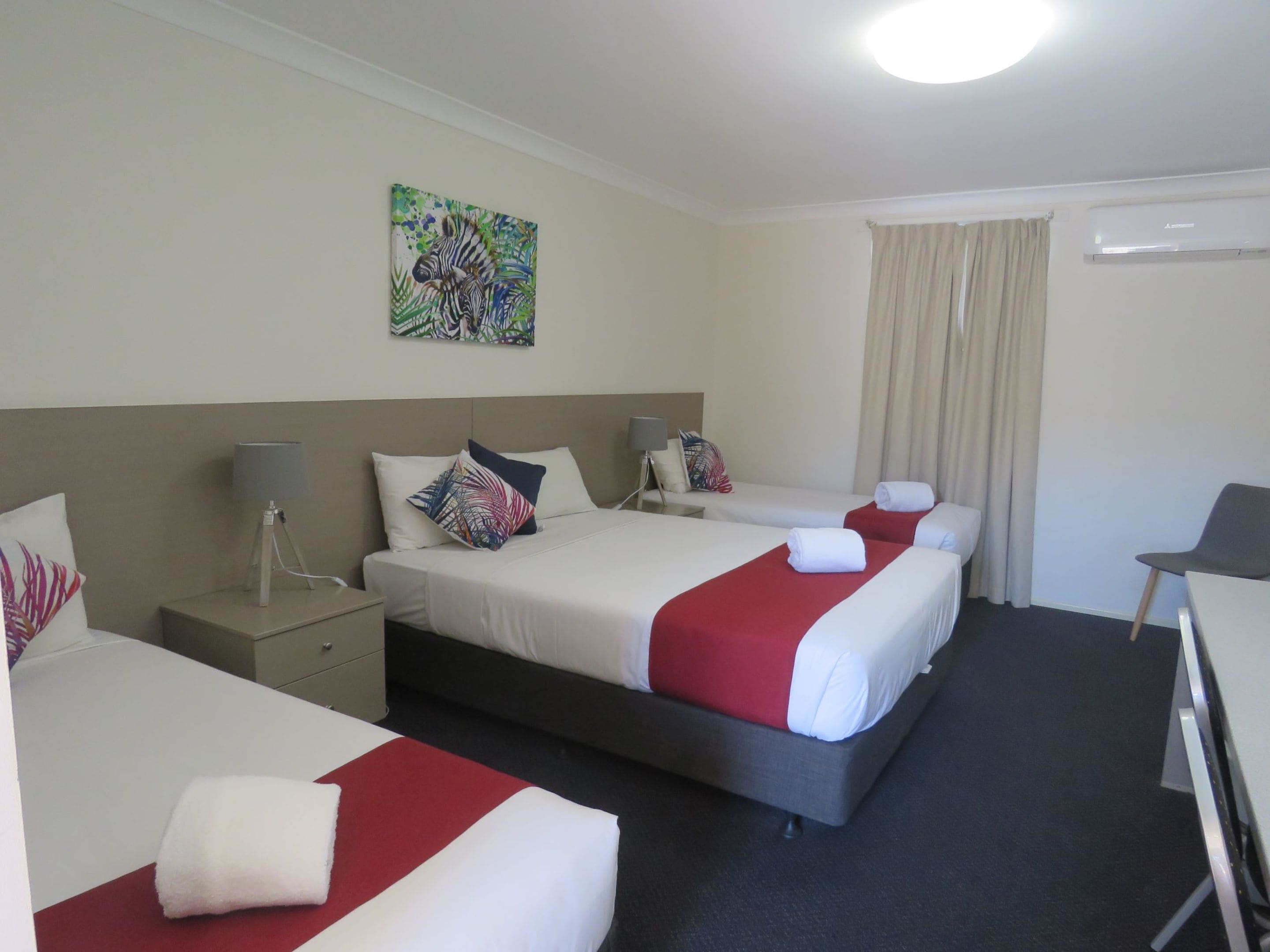A hotel room with two beds, a desk, a chair, a lamp, and a painting on the wall.